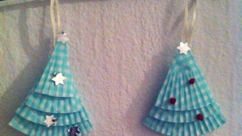 Zwei festliche Weihnachtsbaum Anhänger aus Muffinförmchen hängen an einem schlichten schwarzen Ast an der Wand.