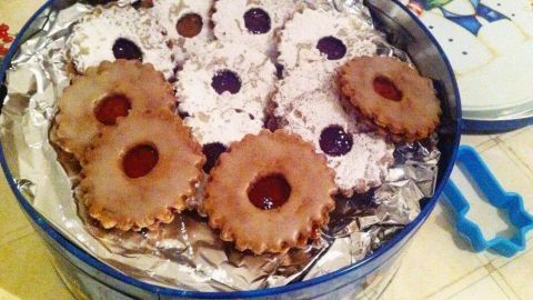 Zimt-Kirsch-Plätzchen liegen ordentlich in einer runden Dose und zeigen eine Mischung aus hellen und dunklen Keksen, verziert mit Marmelade.