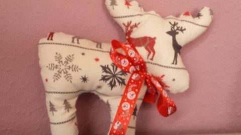Ein niedlicher, genähter Rentier-Halter mit weihnachtlichem Stoff und rotem Band steht auf einem Tisch vor einer rosa Wand.