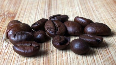 Dunkle Kaffeebohnen liegen verstreut auf einer Holzoberfläche, bereit zum Mahlen für die richtige Kaffeezubereitung.