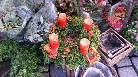Ein adventlicher Kranz mit vier roten Kerzen steht auf einem Tisch, umgeben von festlichem Grün und Weihnachtsdekoration.