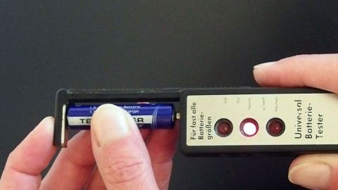Ist die Batterie wirklich schon leer? Ein Batterietester kann Auskunft geben. Ein Prüfer misst eine Batterie mit einem Tester, um ihre Restladung zu bestimmen, auf einem schwarzen Hintergrund.