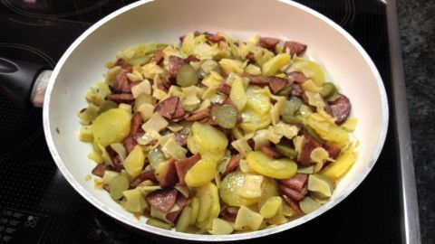 In einer Pfanne braten pikante Reste aus Kartoffeln, Wurst und Gewürzgurken, um ein sättigendes Essen zu kreieren.