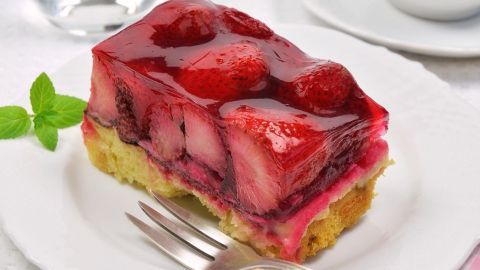 Ein Stück frischer Erdbeerkuchen liegt auf einem weißen Teller, umgeben von einem Glas Wasser und einer Tasse.