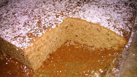 Ein saftiger brauner Kuchen auf dem Blech, mit Puderzucker bestäubt und zur Hälfte angeschnitten.