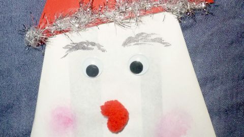 Eine kreativ gestaltete Weihnachtstüte zeigt ein lustiges, bemaltes Gesicht mit einem roten Hut und Bart, dekoriert mit Watte.