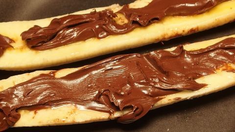 Warme Schoko-Banane liegt auf einem Teller, während cremige Schokolade gleichmäßig darauf verteilt ist.