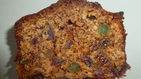 Ein Stück winterlicher Rübli-Früchtekuchen liegt auf einem hellen Untergrund, das Gebäck zeigt karamellisierte Früchte und Nüsse.