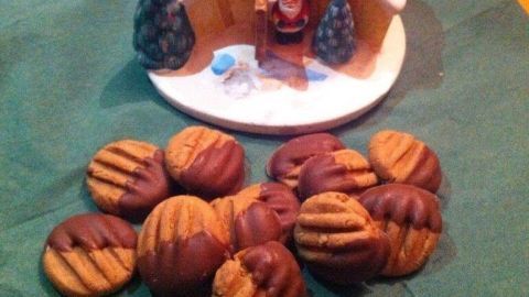 Schokoladeneingepackte Nougattaler liegen verstreut auf einem grünen Tuch vor einem kleinen Winterhäuschen.