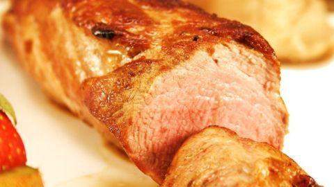 Eine perfekt gegarte Schweinelende liegt auf einem Teller, umgeben von buntem Gemüse und einer cremigen Beilage.