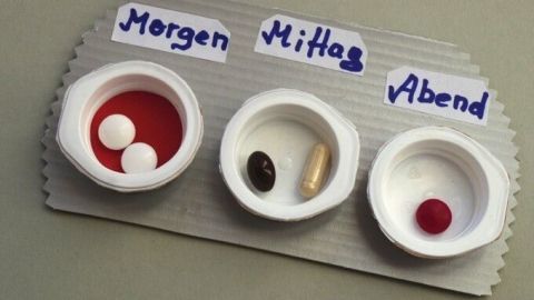 Eine Pillendose aus Milchtüten zeigt drei Fächer mit verschiedenen Medikamenten zur Einnahme: Morgen, Mittag, Abend.