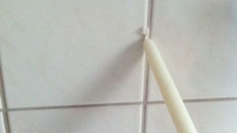 Eine Kerze wird verwendet, um Fliesenfugen zu versiegeln, während sie auf einem hellen Fliesenboden positionsgerecht aufgetragen wird.