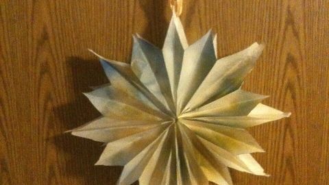 Ein Weihnachtsstern aus Butterbrottüten hängt dekorativ an einer Wand, strahlt festliche Stimmung aus und ist kunstvoll gefaltet.