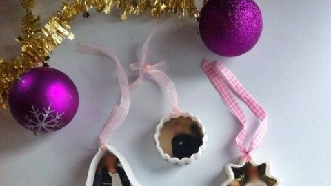 Weihnachtliche Anhänger mit Fotos hängen an einem goldenen Girlande, umgeben von lila Weihnachtskugeln.