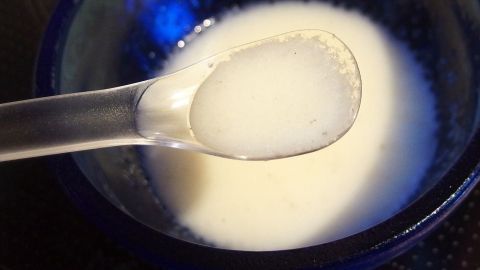 Eine Schüssel mit Aioli-Creme wird mit einem Löffel betrachtet, umgeben von einer dunklen Arbeitsfläche.