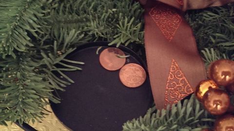 Auf dem Adventskranz stehen leicht schief Kerzen, umgeben von grünem Tannengrün und dekorativem braunem Band.