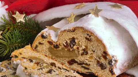 Der Marzipan-Stollen liegt auf einem festlichen Tisch, während ein Stück davon angeschnitten ist, um die Füllung zu zeigen.