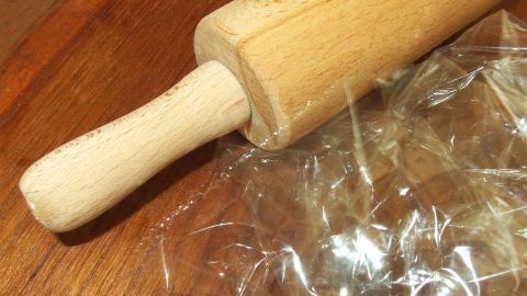 Ein Holzrollingpin liegt auf durchsichtiger Frischhaltefolie, bereit, um Teig ohne Kleben und ohne Mehl auszurollen.