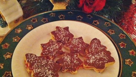 Plätzchen mit Johannisbeergelee sind auf einem festlich dekorierten Teller angerichtet und von Weihnachtsdekoration umgeben.