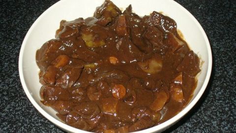 Ein Schüssel Wildschweingulasch ist gefüllt mit dunkler, sämiger Sauce und Gemüse, auf einer schwarzen Arbeitsfläche.