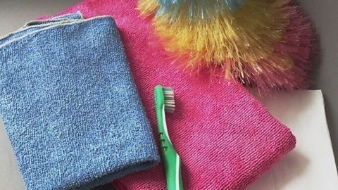 Bunte Reinigungstücher und eine Zahnbürste liegen auf einem Tisch, bereit für die Reinigung von wenig beachteten Stellen im Haushalt.