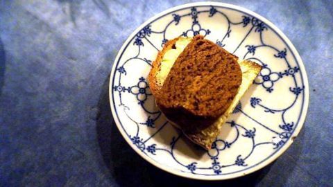 Ein Stück Hamburger Braune Kuchen liegt auf einem verzierten Teller, umgeben von einer dunklen Tischoberfläche.