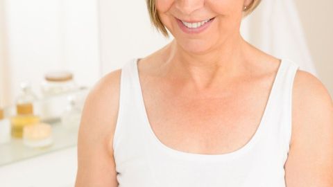 Eine ältere Frau trägt eine Hautpflegecreme auf ihre Hand auf, während sie im Badezimmer entspannende Pflege für den Winter genießt.