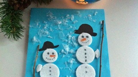 Eine Weihnachtskarte zeigt zwei Schneemänner, die fröhlich unter einem glitzernden Himmel stehen, umgeben von Schnee.