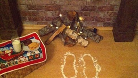 Lustige Schuhabdrücke aus Puderzucker führen zu einem Kamin mit Weihnachtsdeko, während ein Glas Milch daneben steht.