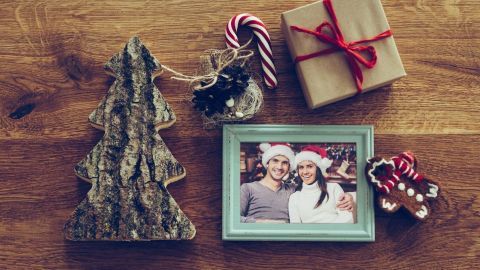 Ein Weihnachtsbaum aus Holz steht neben einem Bildrahmen mit einem Foto von zwei Personen, umgeben von Geschenken und Süßigkeiten.