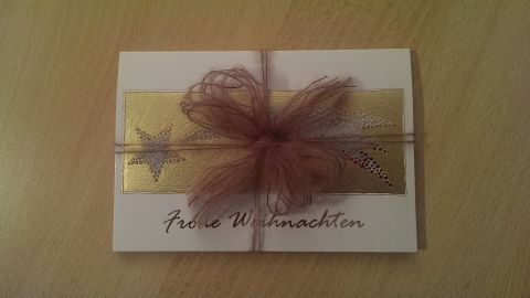 Verleihe deinen Weihnachtskarten mit Wolle einen einzigartigen Touch. Diese kreative Methode sorgt nicht nur für eine liebevolle Verpackung, sondern macht deine Karten auch zu einem besonderen Highlight in der Vorweihnachtszeit. Eine mit Wolle verschlossene Weihnachtskarte liegt auf einem Tisch und ist mit einer braunen Schleife verziert.