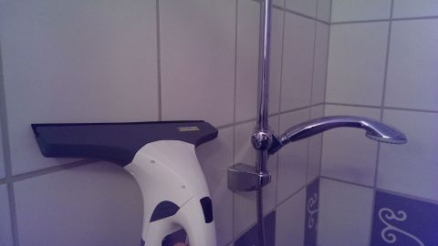 Ein Fenstersauger reinigt Fliesen in einem Badezimmer, um Wasserflecken und Schmutz von den Wandfliesen zu entfernen.