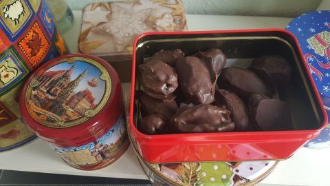Eine rote Dose mit Weihnachtspralinen steht auf einem Regal, umgeben von bunten Keksdosen und einer festlichen Umgebung.