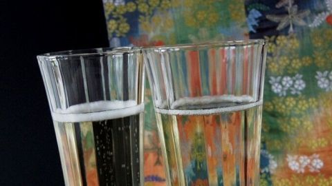 Zwei Gläser Sekt stehen nebeneinander, gefüllt mit alkoholfreiem Sekt, vor einem bunten, gemusterten Hintergrund.