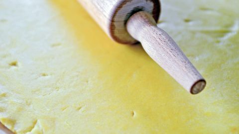 Ein Nudelholz rollt Teig gleichmäßig aus und liegt auf einer gelben Teigfläche in einer hellen Küchensituation.