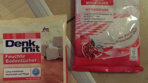 Feuchte Tücher für Fliesen und Laminat liegen auf einem Boden, bereit zum Reinigen, mit Verpackungen im Vordergrund.