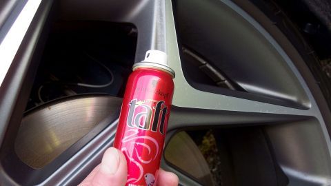 Eine Hand hält eine rote Haarspray-Dose, während sie auf eine Alufelge zielt, um sie zu konservieren.