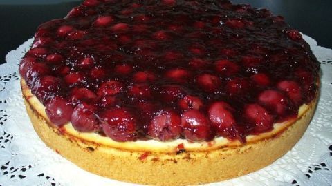 Ein Käsekuchen mit einer dicken Schicht roter Fruchtsoße und Beeren, auf einem dekorativen Tortenteller angerichtet.
