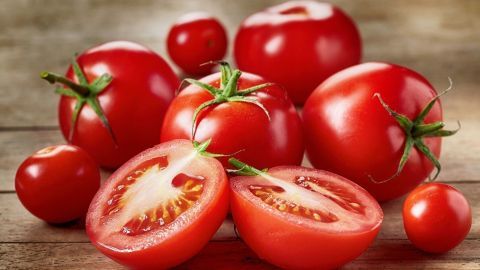 Tomaten liegen frisch auf einem Holztisch, einige sind ganz, andere halbiert, und wirken saftig und reif.
