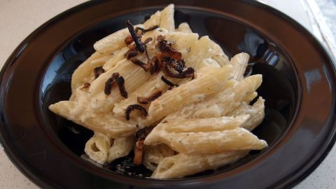 Penne-Nudeln in einer schwarzen Schüssel, angerichtet mit cremiger Creme fraiche und einem Hauch von Kräutern.