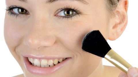 Eine Frau trägt mit einem Pinsel Make-Up auf ihre Wange auf, um einen makellosen Teint zu erzielen und Make-Up Ränder zu vermeiden.