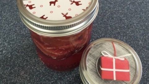 Ein Einmachglas mit roter Marmelade steht auf einem Tisch, dekoriert mit einer festlichen Weihnachtskarten-Übertopf.