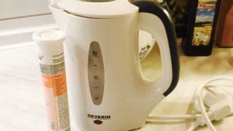 Ein Wasserkocher steht auf einer Arbeitsfläche neben einer Flasche zur Entkalkung. Es wird angezeigt, wie man Kalkablagerungen entfernt.