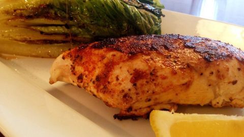 Saftiges Hühnchen liegt neben gebratenem Romanasalat auf einem weißen Teller, garniert mit Zitronenscheibe.