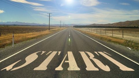 Eine Straße erstreckt sich in die Ferne, mit der Aufschrift "START" in großen Buchstaben auf dem Asphalt unter einem klaren Himmel.