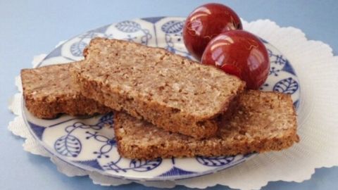 Saftige Nuss-Kokos-Kuchenstücke liegen auf einem blauen Teller mit zwei roten Äpfeln daneben, auf einem Tisch.