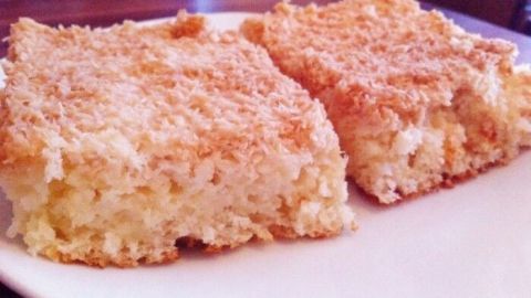Ein saftiger Kokos-Buttermilch-Kuchen liegt auf einem weißen Teller, goldbraun und in Stücke geschnitten, bereit zum Genießen.