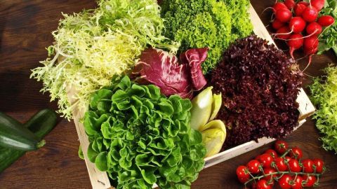 Frischer Salat in einer Kiste, bunt gemischt mit verschiedenen Blattgemüsen und roten Kirschtomaten auf einem Holztisch.