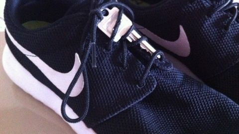 Schwarze Jogging-Schuhe liegen auf einem Tisch, während der Schnürsenkel locker auf dem Schuhblatt hängt.