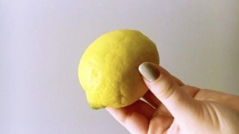 Eine Hand hält eine frische Zitrone, die zum Reinigen der Metalloberfläche in der Küche verwendet wird.